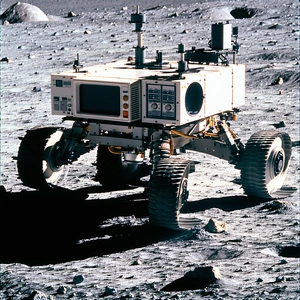 A Robotic Vehicle Is Parked On A Rocky Surface, Possibly On The Moon