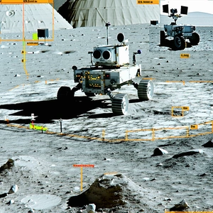 A White Robotic Vehicle, Possibly A Rover, Driving Across A Rocky Terrain